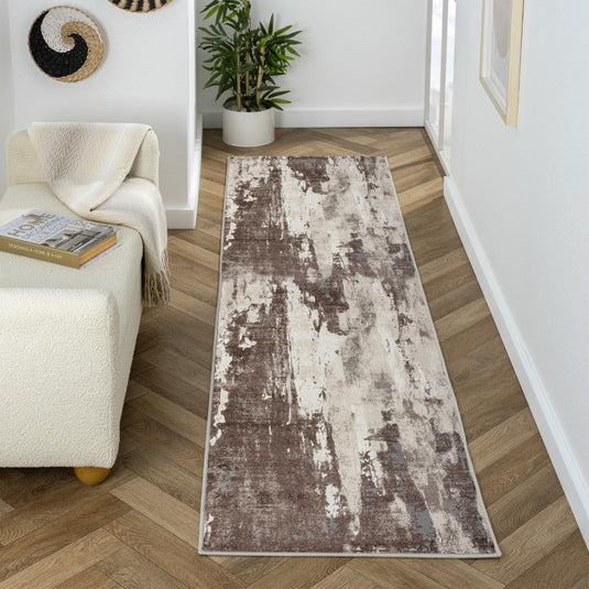 Long rectangular brown rug on a wooden floor with a white wall and plant in the background