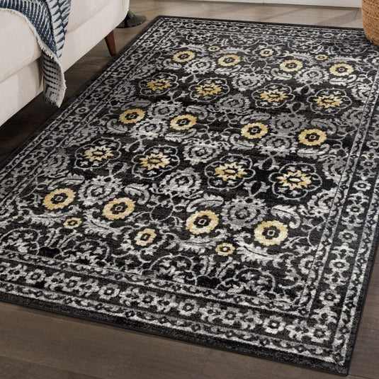 Decorative floral rug with black, gray, and yellow pattern on a wooden floor.
